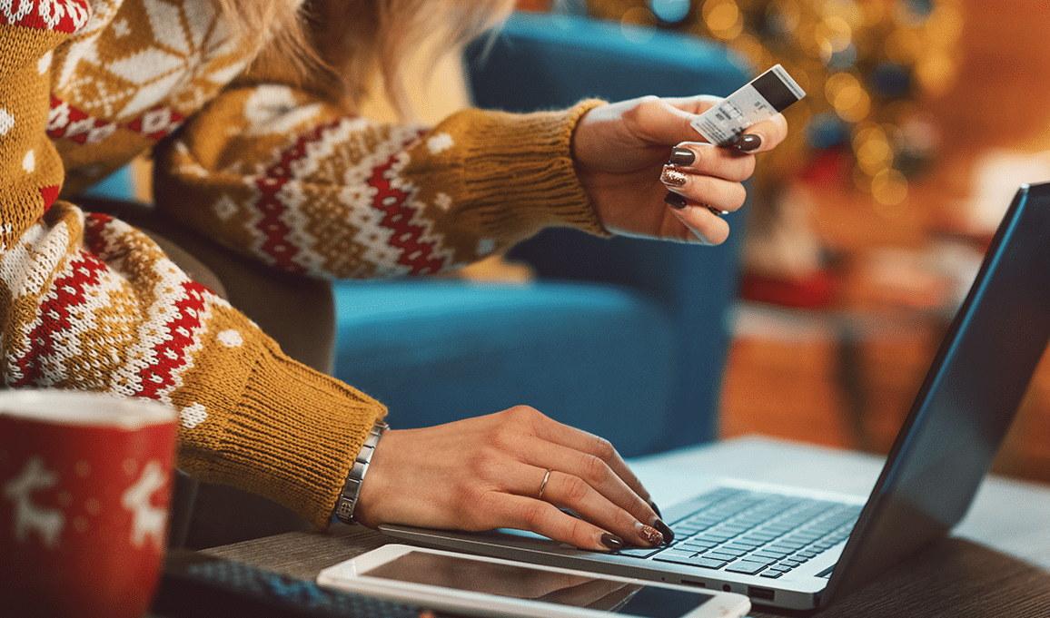 a woman in a sweater shopping online with her credit card out as if she's about to pay.